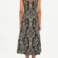 A person stands facing away in the Ulla Johnson Natali Tank Dress—sleeveless, black, with a beige floral leaf print—paired with brown heeled sandals against a plain white background.