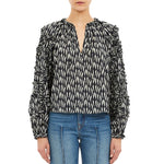 A person wearing the Ulla Johnson Azrou Blouse—a black and white patterned top with ruffled long sleeves—paired with blue jeans, shown from the waist up.
