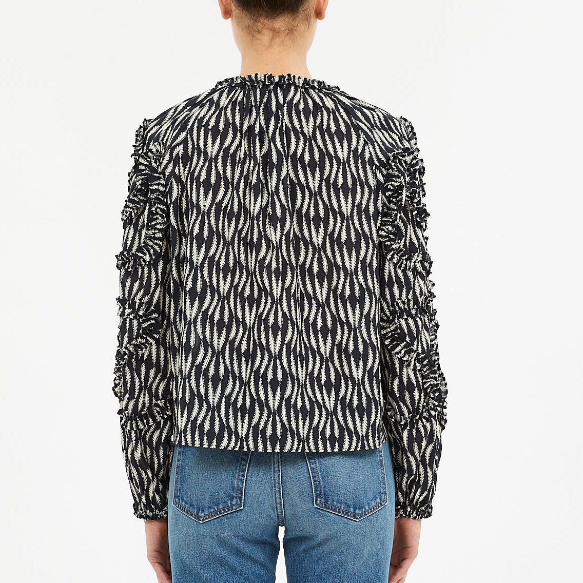 A person, shown from the back against a plain white background, wears the Ulla Johnson Azrou Blouse—a black and white patterned, long-sleeve top with ruched sleeves—paired with blue jeans.