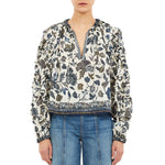A person is wearing the Ulla Johnson Azrou Blouse, a long-sleeve, floral-patterned V-neck top, paired with blue jeans and shown from the front.
