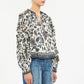 A person is shown from shoulders to hips wearing the Ulla Johnson Azrou Blouse, a long-sleeve, floral-patterned top with ruffled details, paired with blue jeans.