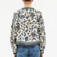 A person is seen from the back wearing the Ulla Johnson Azrou Blouse, a long-sleeved, floral-patterned top with ruffled arm details, paired with blue jeans.