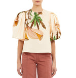 Someone wearing the Ulla Johnson Ravena Puff Sleeve Top, a cream-colored blouse with a large floral print, paired with high-waisted pink pants.