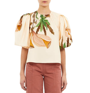 Someone wearing the Ulla Johnson Ravena Puff Sleeve Top, a cream-colored blouse with a large floral print, paired with high-waisted pink pants.