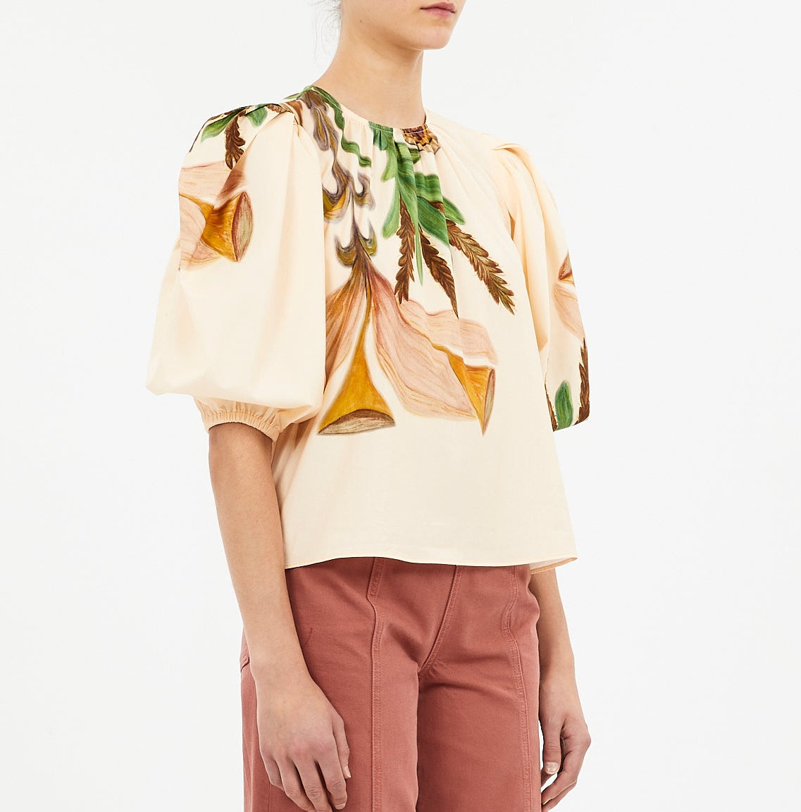Someone wearing the Ulla Johnson Ravena Puff Sleeve Top, a cream floral blouse with short puffed sleeves, paired with high-waisted pink pants.