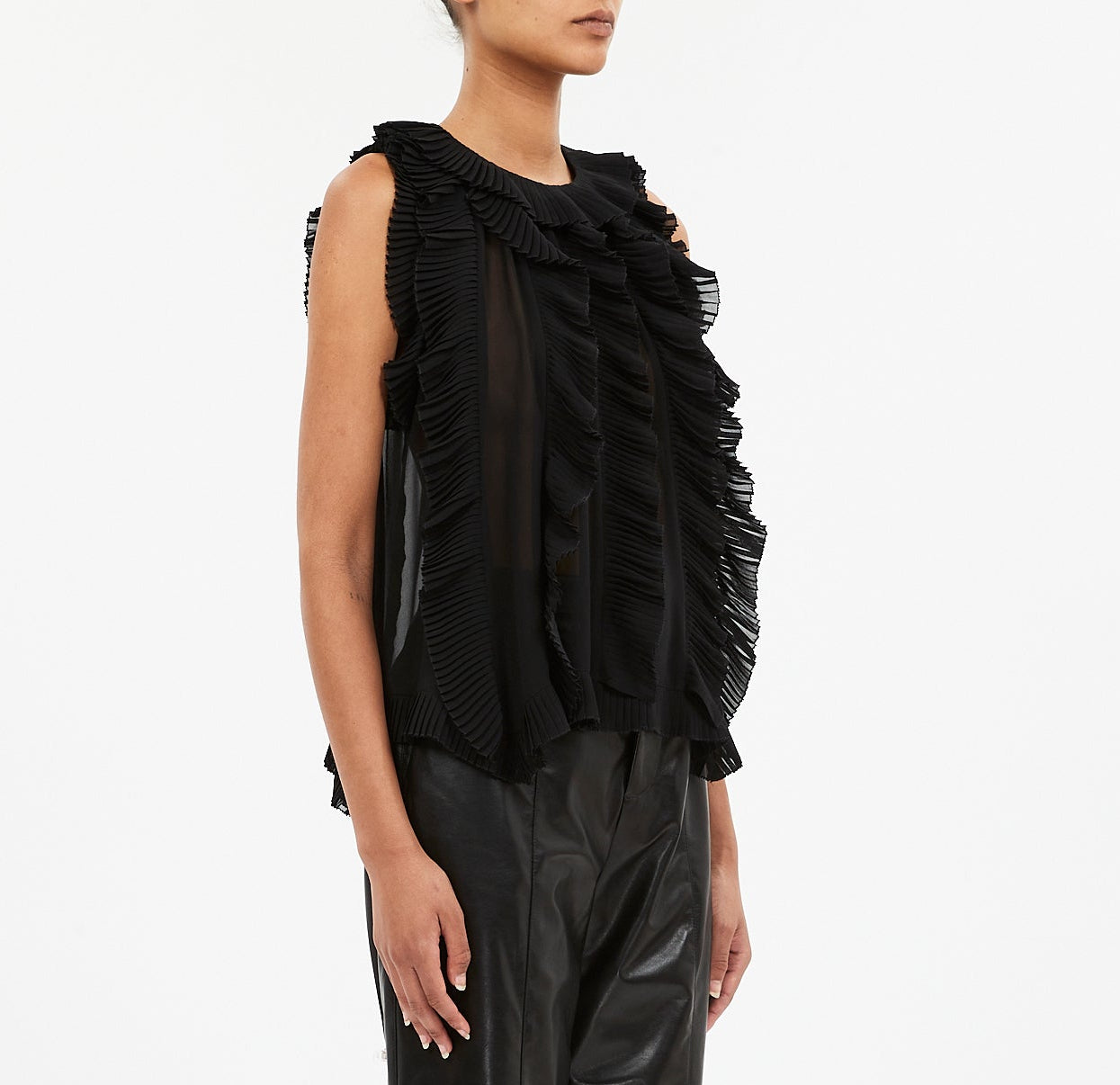 A person wears the Ulla Johnson Sabra Cascading Ruffle Top, a sleeveless black silk top with layered ruffles, paired with black leather pants and photographed against a plain white background.
