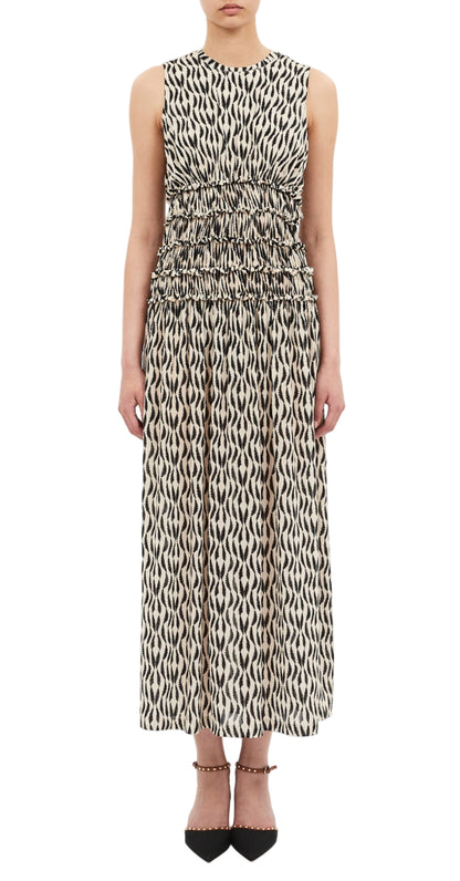 A person wearing the Ulla Johnson Kamaria Dress—a sleeveless, ankle-length black and white patterned dress with a gathered waist—paired with black pointed-toe shoes.