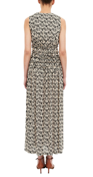 A person is seen from the back wearing the Ulla Johnson Kamaria Dress—a sleeveless, long black and white patterned dress with a gathered waist—paired with brown heeled sandals.