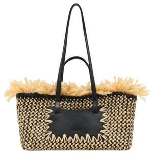 The Ulla Johnson Lali Small East West Tote is a rectangular hand-woven straw bag with black handles, a black rectangular patch, and decorative straw fringe along the top.