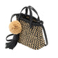 The Ulla Johnson Raffia Mini Crossbody is a small hand-woven tote with a black and beige checker pattern, black handles, and a black leather tassel accented by a large beige pom-pom.