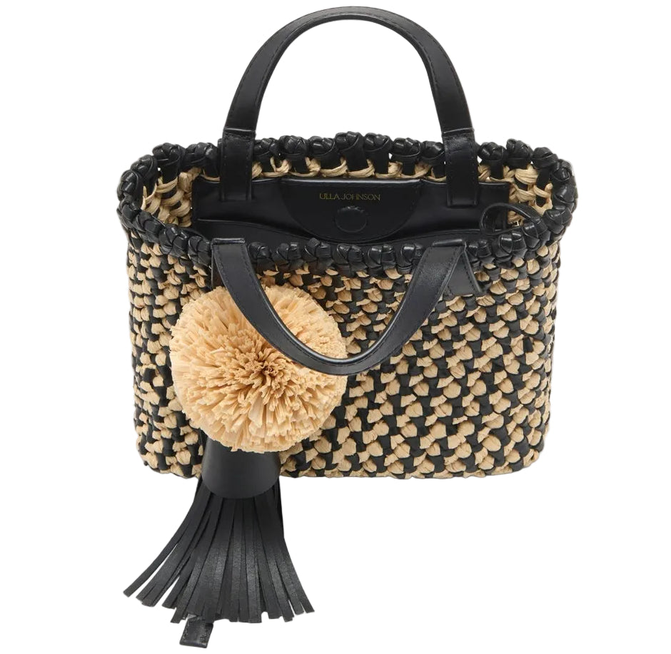 The Ulla Johnson Raffia Mini Crossbody is a hand-woven handbag featuring black and beige materials, black leather handles, a large beige pom-pom, and a black leather tassel—perfect as a chic mini tote for any occasion.