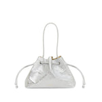 The Mansur Gavriel Drawstring Crinkle Pouchette is a metallic silver compact handbag with two side pull cords and a thin shoulder strap, crafted from premium leather and shown against a white background.