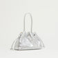 The Mansur Gavriel Drawstring Crinkle Pouchette is a small metallic silver Italian leather handbag with two handles and a gathered, textured design, shown against a plain light background.
