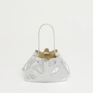The Mansur Gavriel Drawstring Crinkle Pouchette is a small silver metallic bucket bag made from premium leather with thin handles, shown against a plain white background.