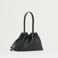 The Mansur Gavriel Drawstring Pouchette is a compact black handbag crafted from Italian leather, featuring a curved top handle—ideal for carrying your essentials in style. Displayed against a plain white background.