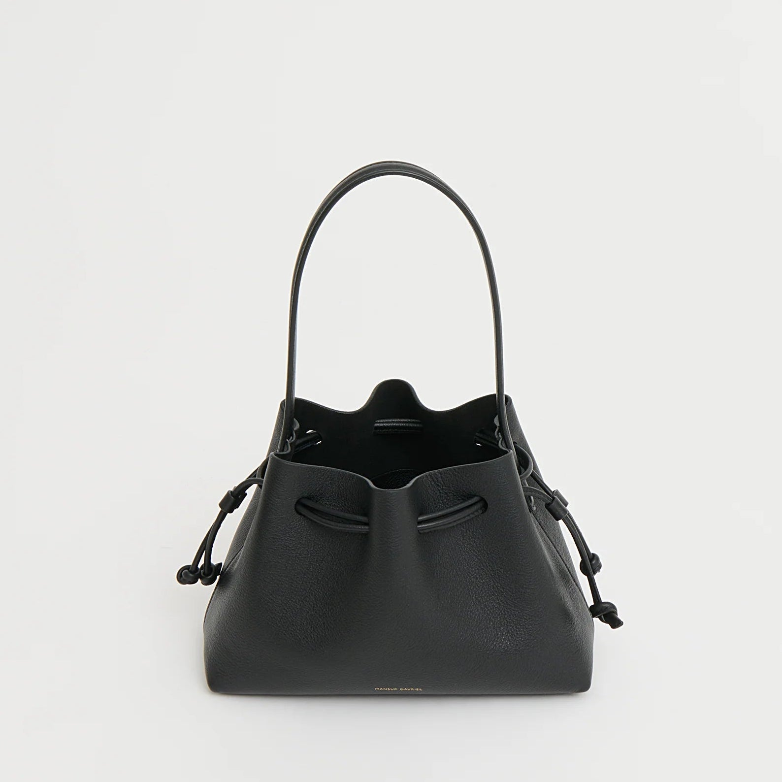 The Mansur Gavriel Drawstring Pouchette is a black Italian leather bucket bag with two handles and a drawstring closure, ideal for essentials. Shown against a plain white background.
