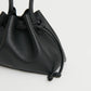 A close-up of the Mansur Gavriel Drawstring Pouchette, crafted from black Italian leather with knotted drawstring ends, shown against a plain light background.
