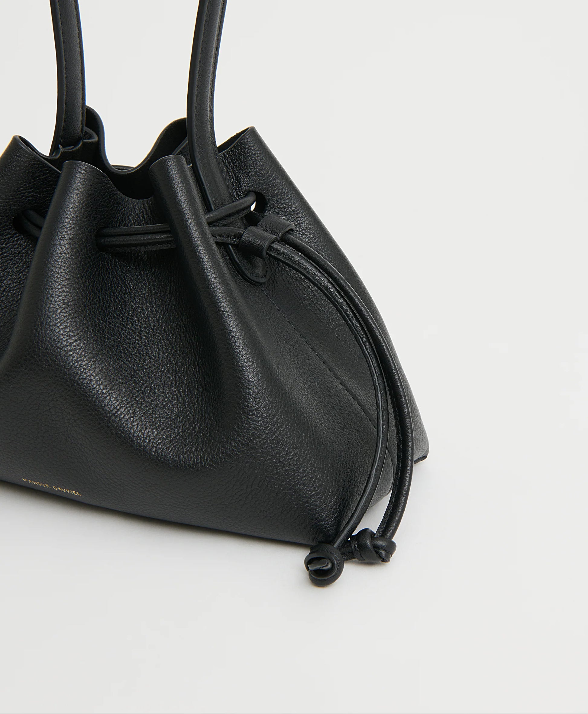 A close-up of the Mansur Gavriel Drawstring Pouchette, crafted from black Italian leather with knotted drawstring ends, shown against a plain light background.