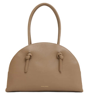 The Fortuna Bowling Bag by Mansur Gavriel features taupe Italian leather, a rounded top, two handles, knotted strap details, and a gold embossed logo near the base.