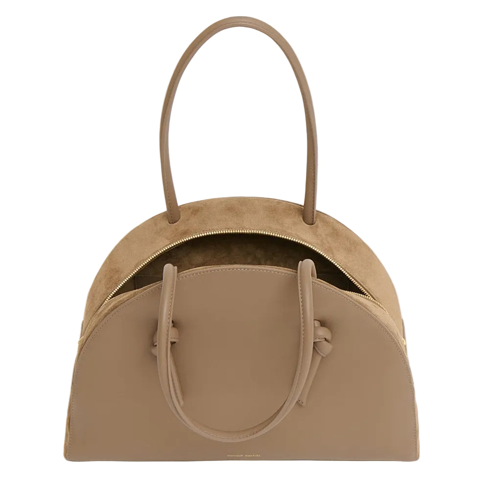 The Fortuna Bowling Bag by Mansur Gavriel is a taupe Italian leather top-handle bag featuring two handles, a curved top, and a partially open zipper that reveals a spacious suede interior.