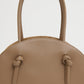 A close-up view of the Mansur Gavriel Fortuna Bowling Bag, a tan Italian leather top-handle bag featuring two handles and knotted strap details, shown against a plain background.