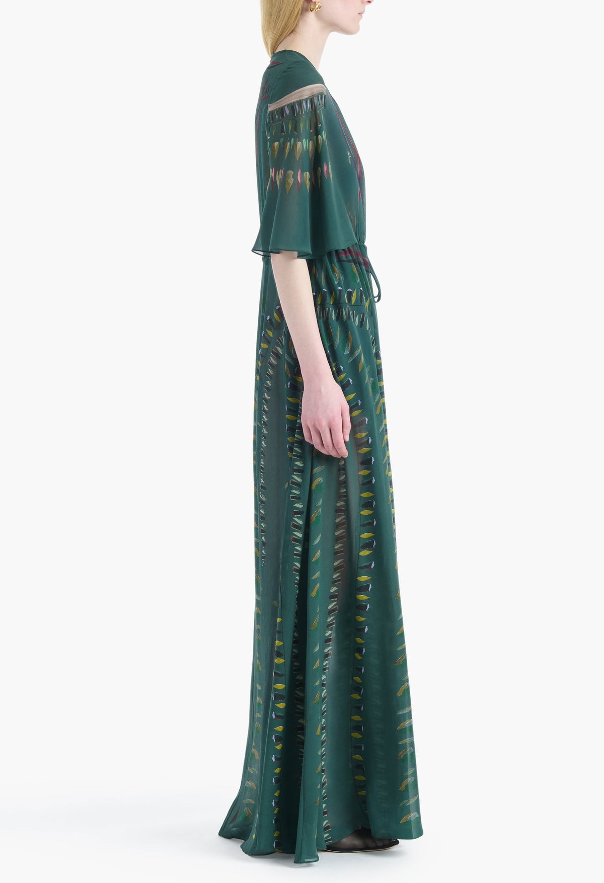 A woman in an elegant, floor-length Thessaly Dress by Altuzarra—featuring a green hue, short sleeves, and a subtle vertical pattern—stands in profile against a white background.