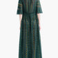A person is seen from the back against a plain white background, wearing the Thessaly Dress by Altuzarra—a long, sheer dark green silk dress featuring botanical patterns.