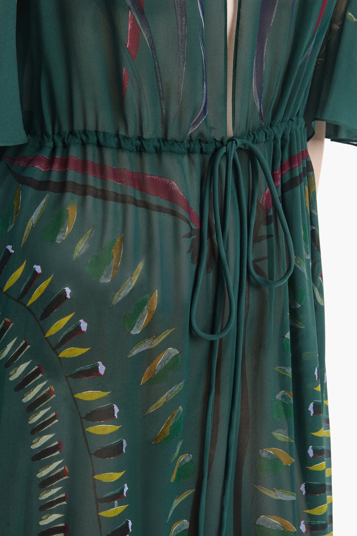 Close-up of the Thessaly Dress by Altuzarra—an elegant green sheer dress with a drawstring waist, featuring a leafy and abstract multicolored pattern.
