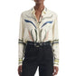 Wearing the Altuzarra Chika Top—a cream-colored silk blouse featuring abstract floral patterns and a concealed button closure—tucked into high-waisted black pants and accessorized with a black belt.