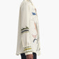 A person wearing the Altuzarra Chika Top, a relaxed long-sleeve cream silk blouse with colorful embroidered designs on the sleeves, front, and cuffs, is shown from the side against a white background.