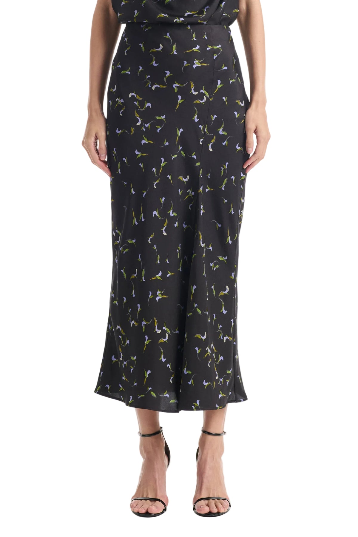 A person wearing the Altuzarra Casey Skirt—a black midi skirt featuring a small floral print and a streamlined silhouette—paired with black strappy sandals.