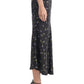 A person shown in profile wears the Altuzarra Casey Skirt—a black, mid-length skirt with a floral pattern—paired with black high-heeled sandals. The midi skirt by Altuzarra creates a streamlined silhouette that flatters the figure.