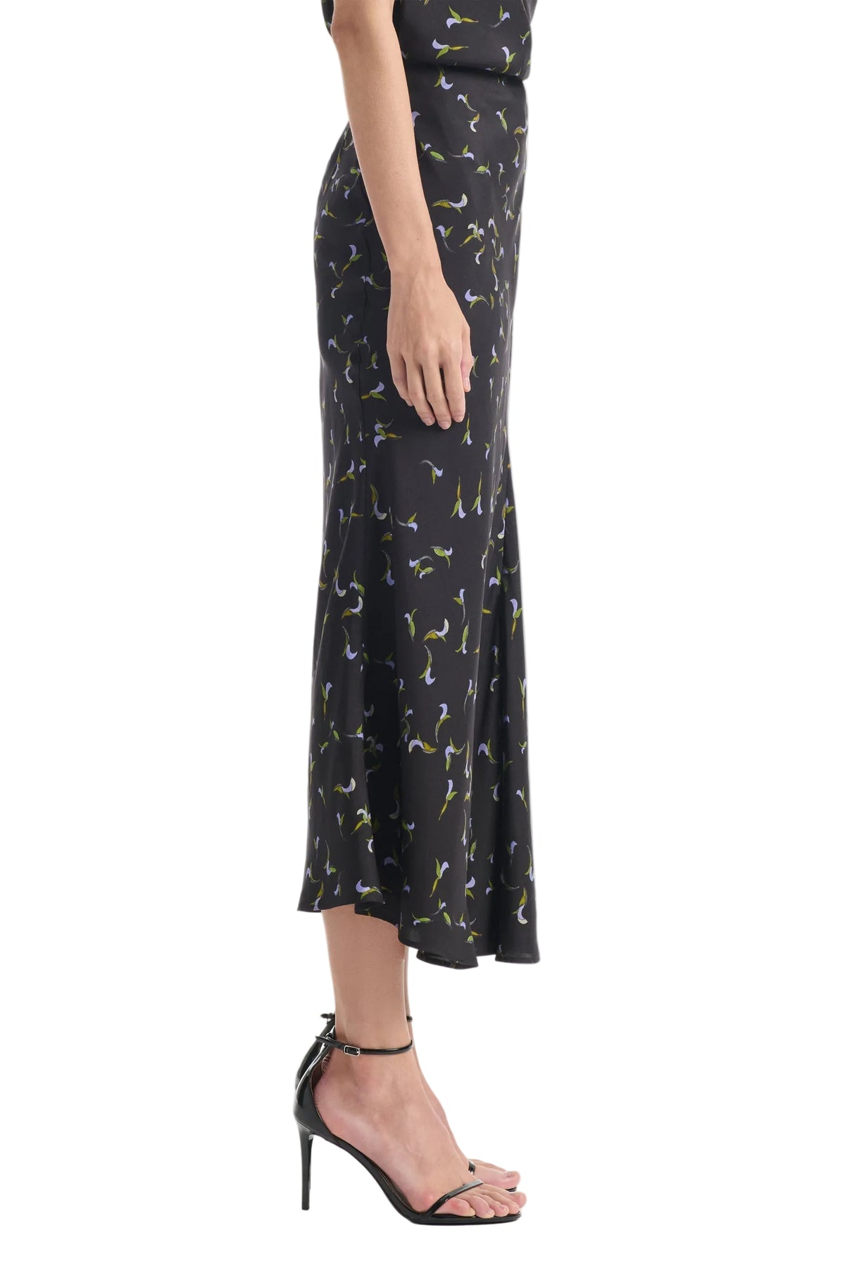 A person shown in profile wears the Altuzarra Casey Skirt—a black, mid-length skirt with a floral pattern—paired with black high-heeled sandals. The midi skirt by Altuzarra creates a streamlined silhouette that flatters the figure.