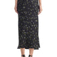 A person is shown from the back wearing the Altuzarra Casey Skirt, a black midi skirt with a small floral print and streamlined silhouette, paired with black high-heeled sandals.