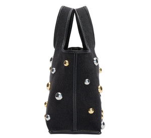 Side view of the 3.1 Phillip Lim Washed Denim Mini Market Tote, featuring black fabric with white stitching and chic gold and silver dome stud accents.