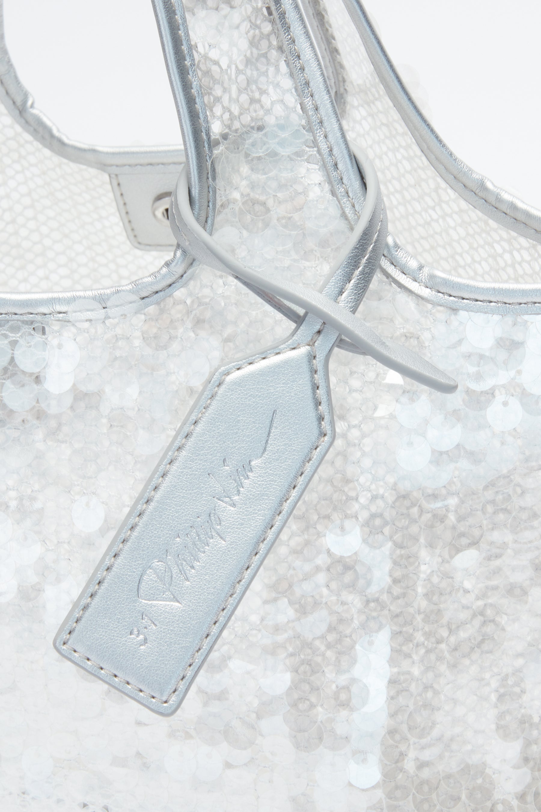 Close-up of the 3.1 Phillip Lim Mesh Sequin Mini Market Tote in silver sequin mesh, accented with a matching metallic leather tag on the handle and elegant cursive text.