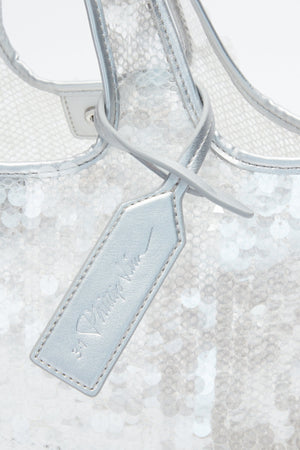 Close-up of the 3.1 Phillip Lim Mesh Sequin Mini Market Tote in silver sequin mesh, accented with a matching metallic leather tag on the handle and elegant cursive text.