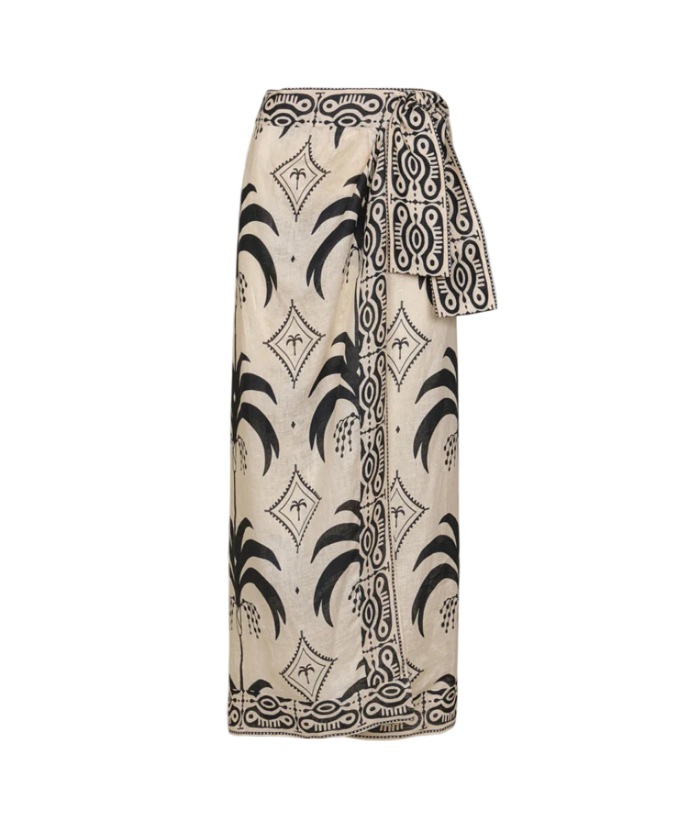 The Significado Poderoso Ankle Skirt by Johanna Ortiz is a beige linen wrap skirt with black tropical and geometric patterns and a wide waist sash for a bold detail.