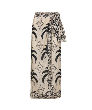 The Significado Poderoso Ankle Skirt by Johanna Ortiz is a beige linen wrap skirt with black tropical and geometric patterns and a wide waist sash for a bold detail.