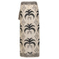 The Johanna Ortiz Significado Poderoso Ankle Skirt is a beige linen wrap skirt with a black palm tree print and geometric border, featuring a straight silhouette, displayed against a white background.