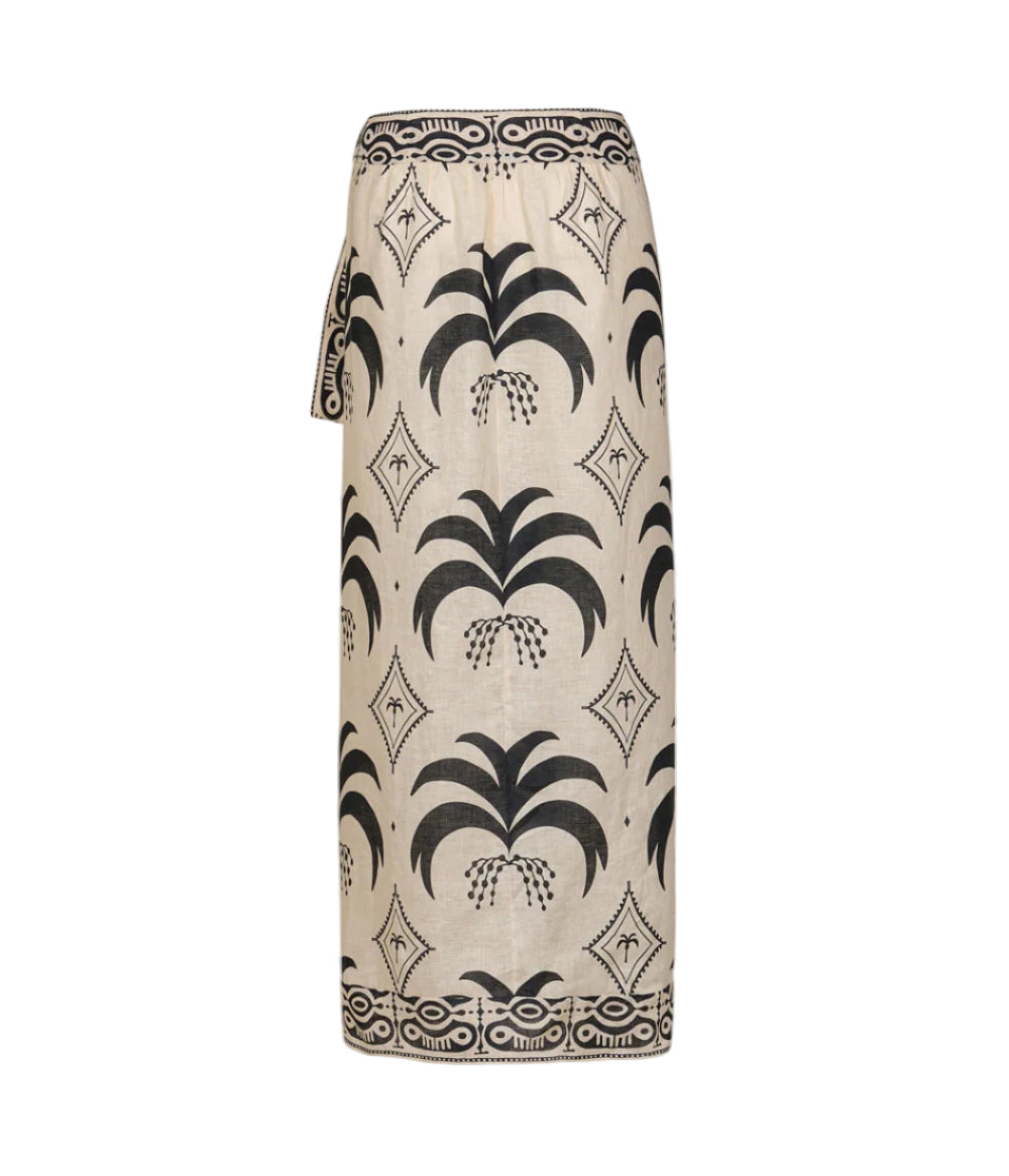The Johanna Ortiz Significado Poderoso Ankle Skirt is a beige linen wrap skirt with a black palm tree print and geometric border, featuring a straight silhouette, displayed against a white background.