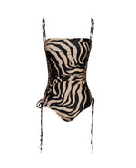 The Palms Tarangire One Piece by Johanna Ortiz features a black and beige zebra print, adjustable shoulder straps, and ruched sides with side ties for a flattering silhouette.