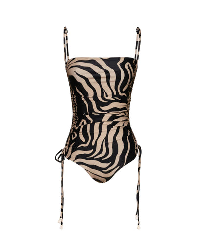 The Palms Tarangire One Piece by Johanna Ortiz features a black and beige zebra print, adjustable shoulder straps, and ruched sides with side ties for a flattering silhouette.