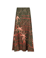 The Encanto De Isla Ankle Skirt by Johanna Ortiz features a high-waisted, ankle-length silhouette with a dark green base, adorned with pink and red palm tree and building prints.