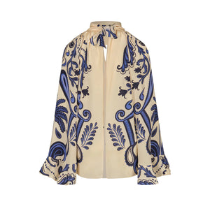 The Ritmo Sol Top by Johanna Ortiz is a beige silk blouse featuring a blue and black ornate floral print, high neck tie detail, relaxed fit, and loose, voluminous sleeves.