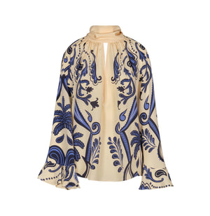 The Ritmo Sol Top by Johanna Ortiz is a cream silk blouse with a relaxed fit, keyhole neckline, blue and black botanical print, voluminous sleeves, and flared cuffs.
