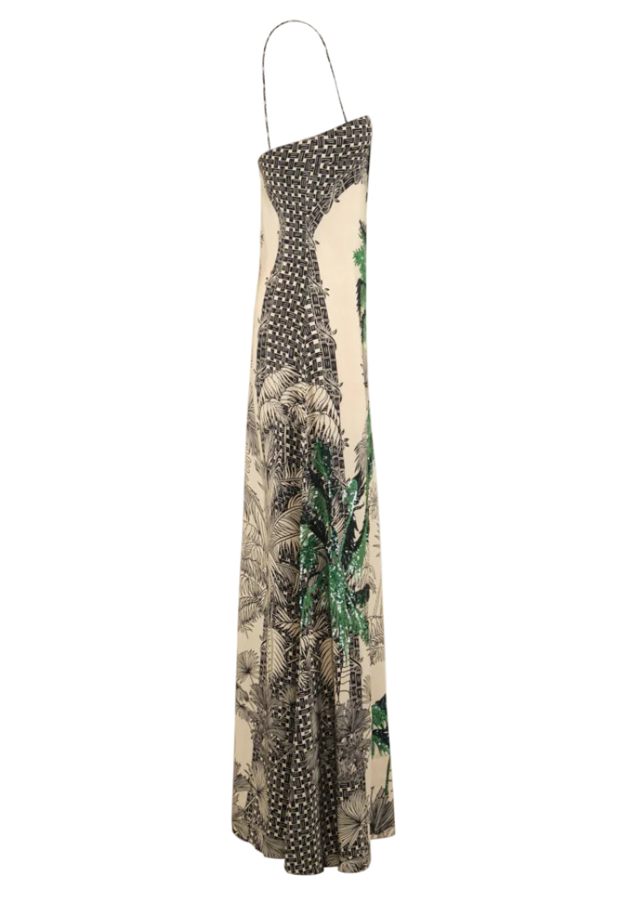 The Simbologia Floral Maxi Dress by Johanna Ortiz features a beige and black one-shoulder design with tropical motifs, a palm tree print, and a thin shoulder strap.