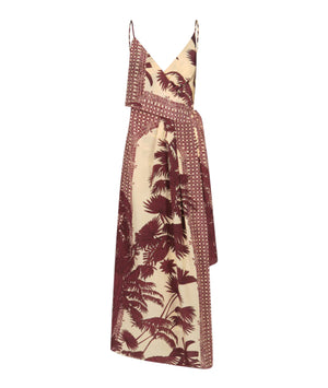 The Nouvel Arome Maxi Dress by Johanna Ortiz features a sleeveless beige tropical print with burgundy palm motifs, a V-neckline, thin straps, and an asymmetric layered front.