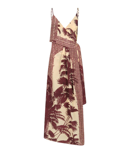 The Nouvel Arome Maxi Dress by Johanna Ortiz features a sleeveless beige tropical print with burgundy palm motifs, a V-neckline, thin straps, and an asymmetric layered front.