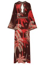 The Leyenda Del Tiempo Maxi Dress by Johanna Ortiz features long sleeves, a brown base with red and beige tropical palm tree and star motifs, wide sleeves, and a keyhole neckline accented with decorative trim.